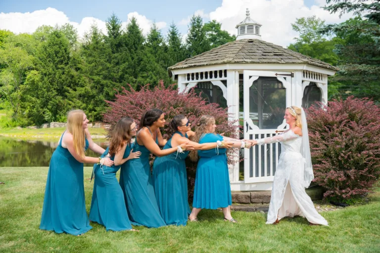 Bride and bridesmaids sharing a playful moment beside a gazebo